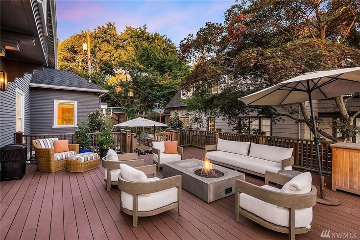 a deck with chairs, couches and an umbrella on it in front of a house