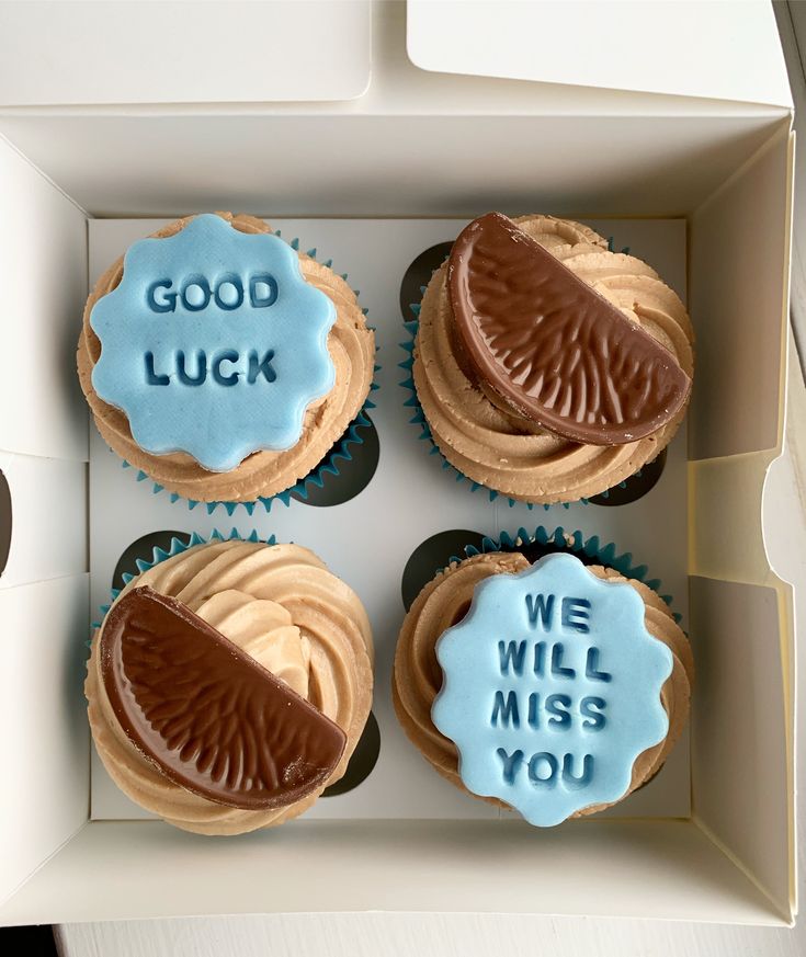 four decorated cupcakes in a box with good luck and we will miss you written on them