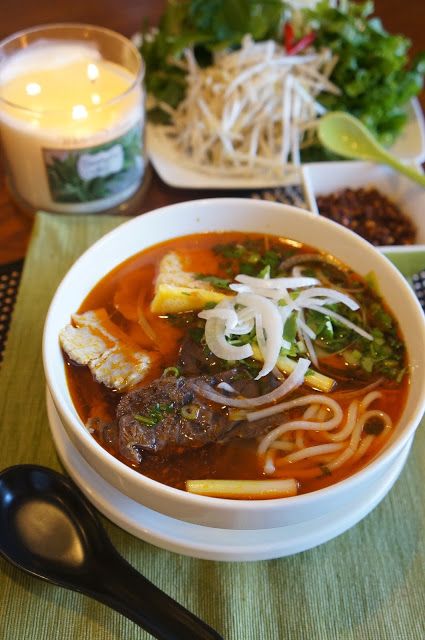 a bowl of soup with meat, noodles and vegetables in it next to a candle