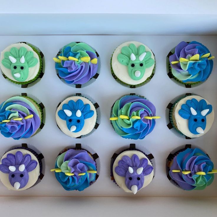 twelve decorated cupcakes in a box with blue and green frosting on them