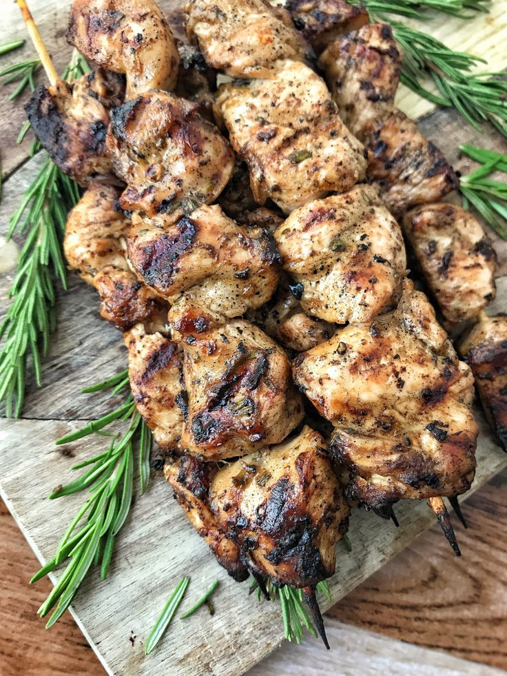 grilled chicken skewers on a wooden cutting board with rosemary sprigs