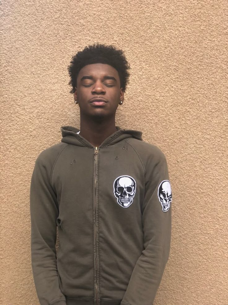 a young man standing in front of a wall wearing a hoodie with skulls on it