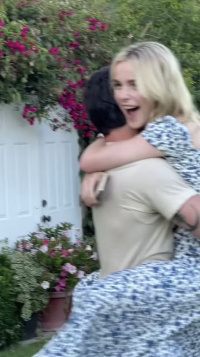 two women hugging each other in front of flowers