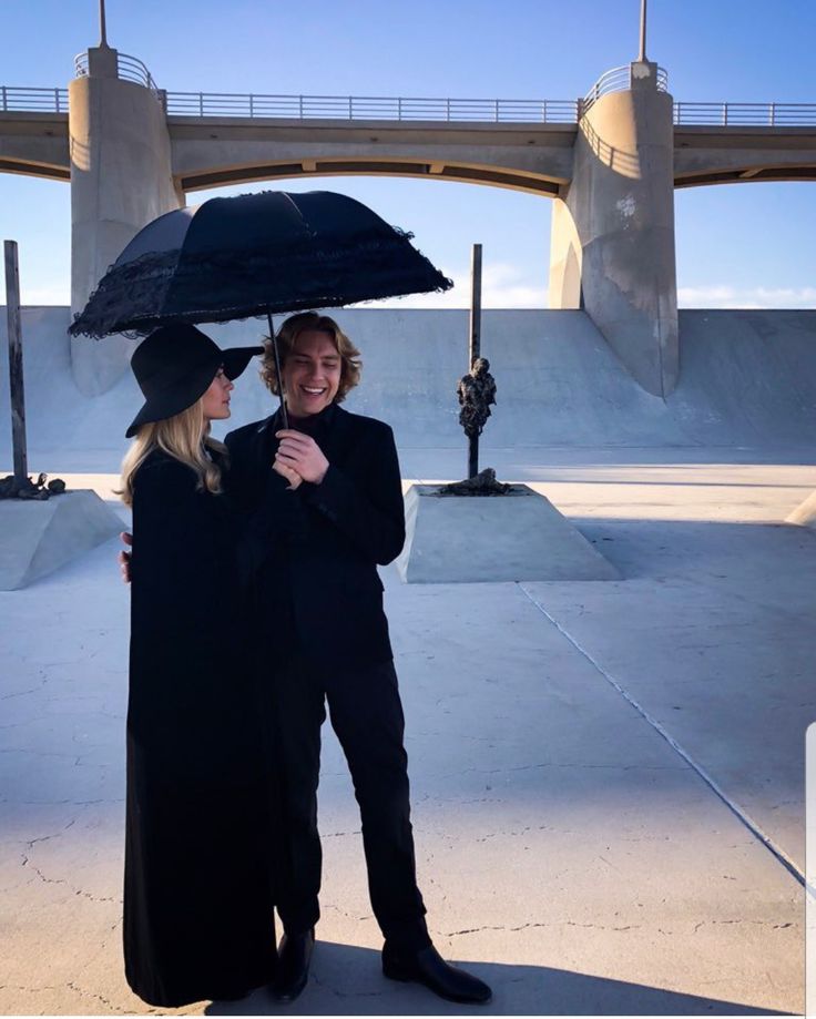 two women are standing under an umbrella in the middle of a skate park, talking