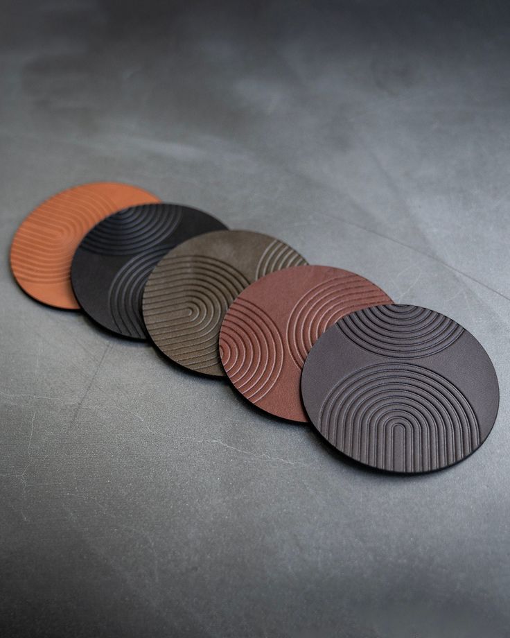 five circular coasters sitting on top of a gray surface with orange and black circles