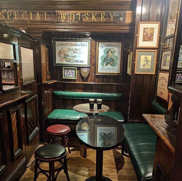 the inside of a restaurant with wooden walls and green leather booths, tables and stools