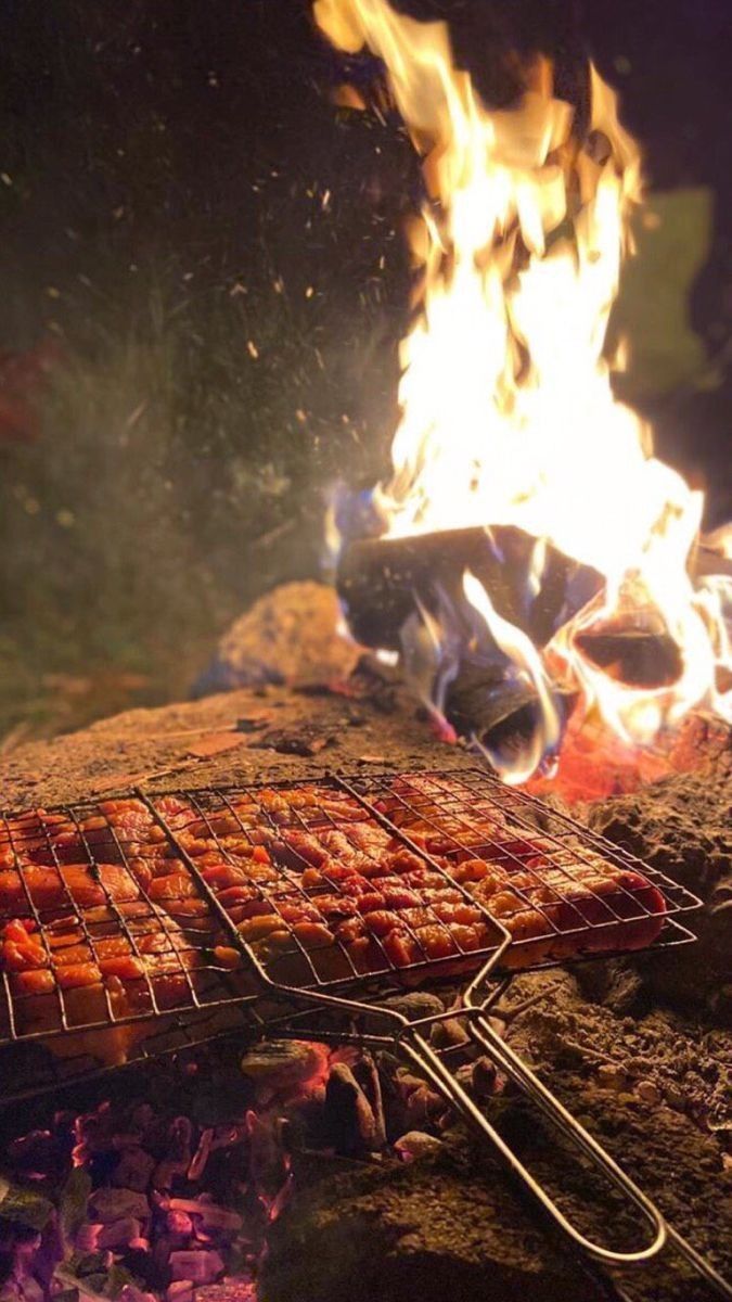 a bbq grill with hot dogs cooking on it's side and flames in the background