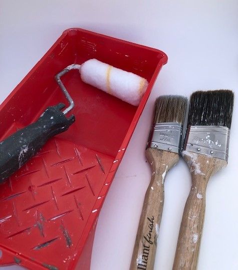 two paintbrushes in a red container next to some other tools