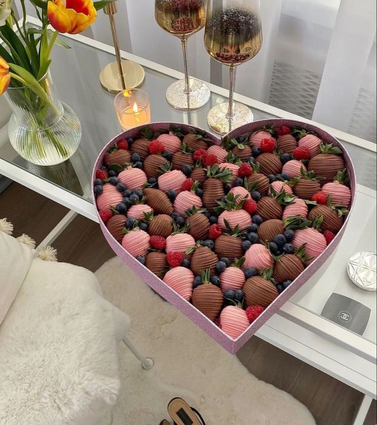 a heart shaped box filled with chocolate covered strawberries and berries next to two wine glasses