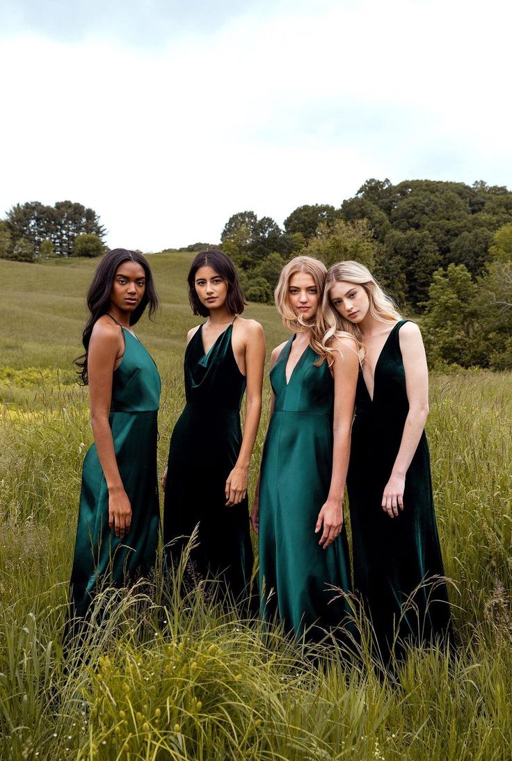 four women in long dresses standing in tall grass