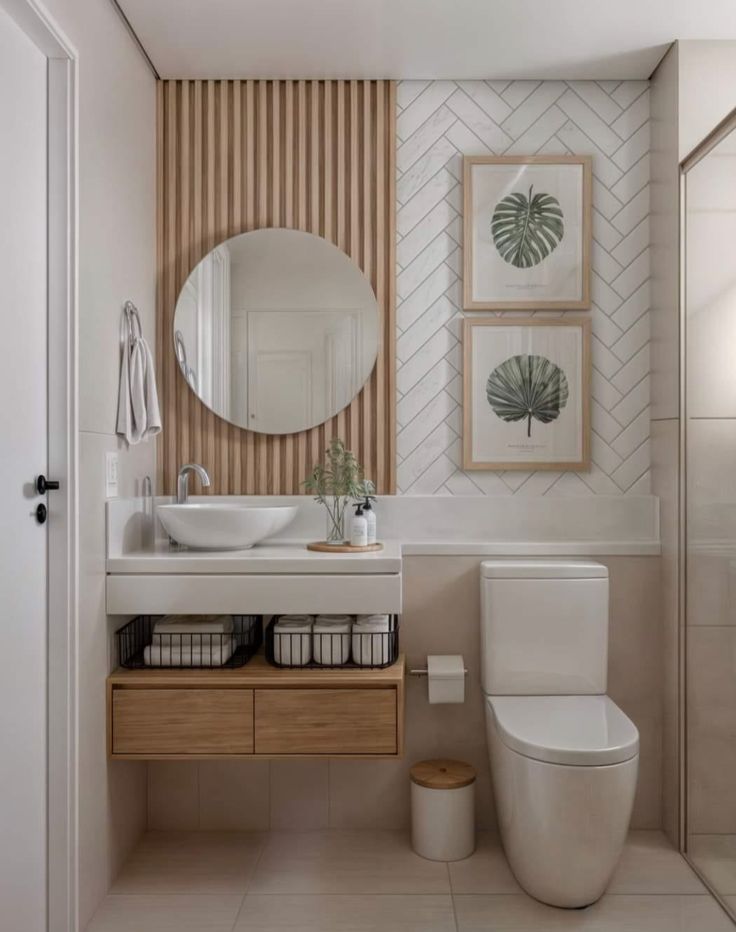 a white toilet sitting next to a bathroom sink under a round mirror on top of a wooden cabinet