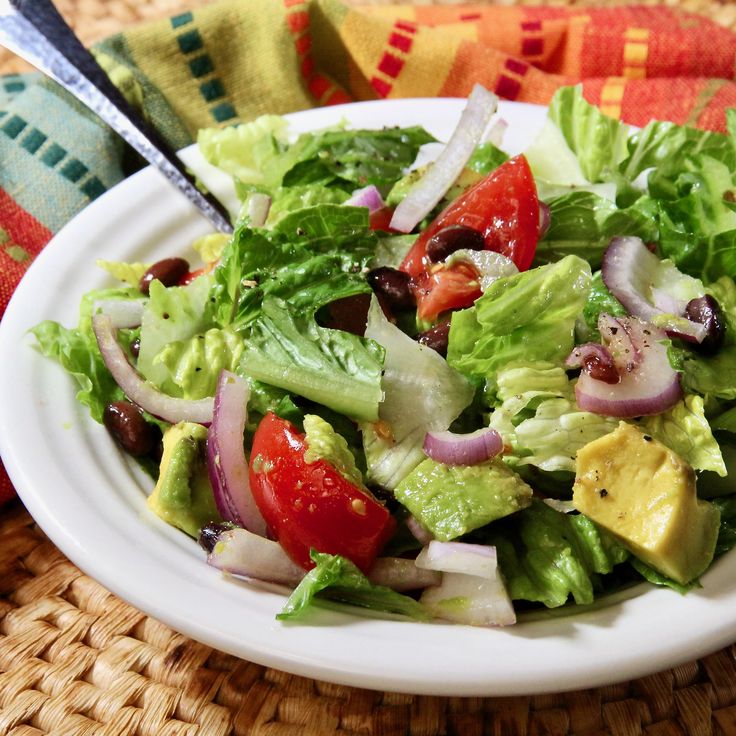 a salad with lettuce, tomatoes, onions and olives on a white plate