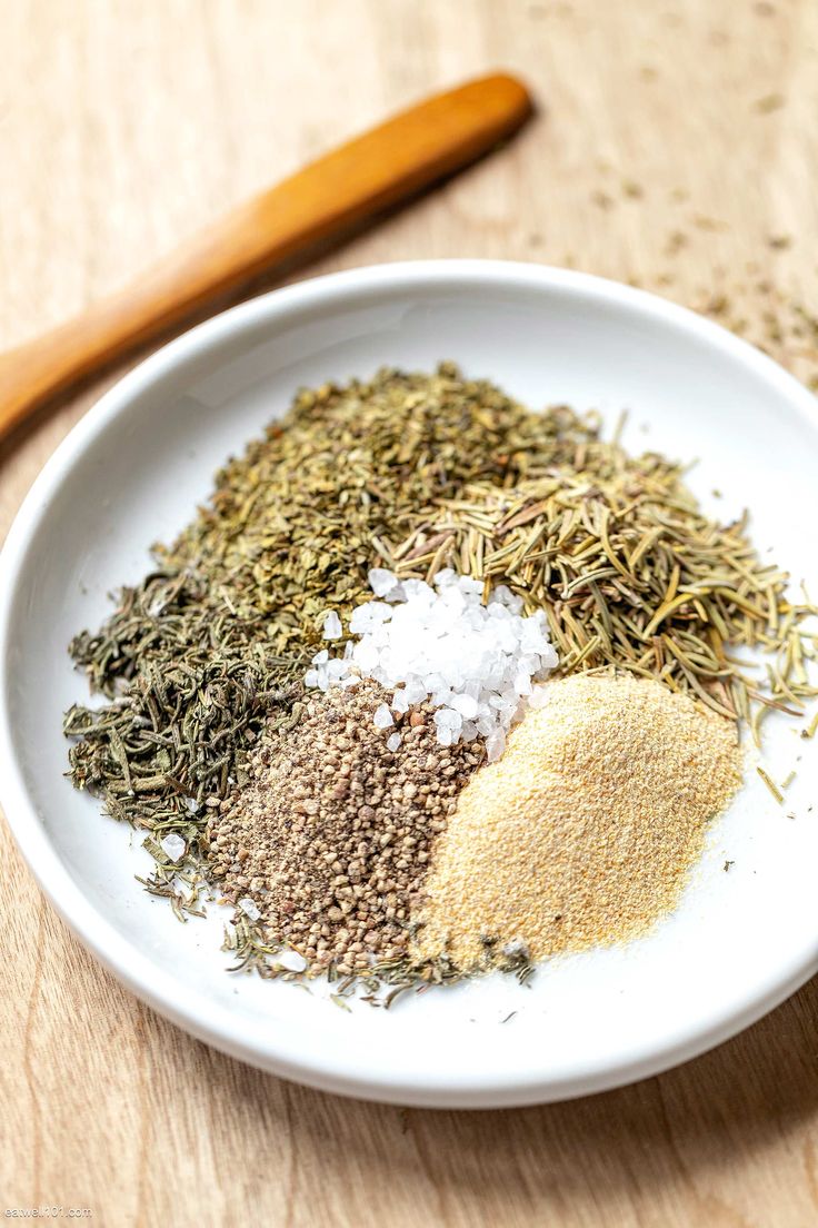 a white bowl filled with spices next to a wooden spoon on top of a table