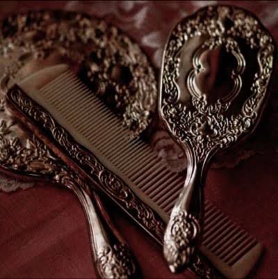 two silver combs sitting on top of a red table cloth next to a mirror