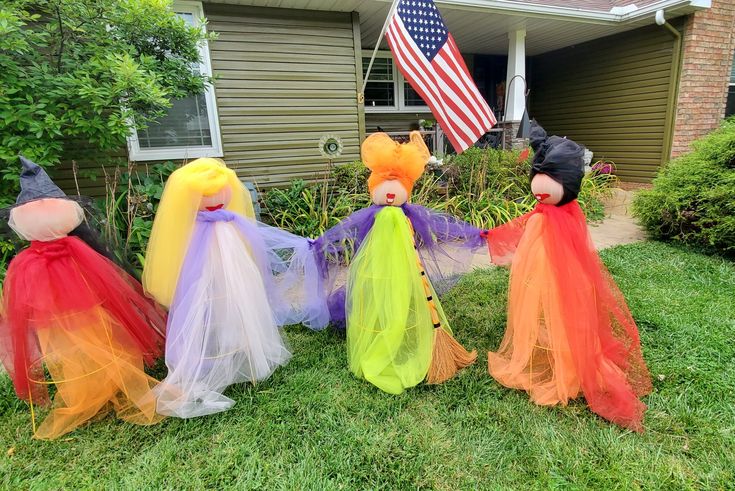 four colorful halloween decorations in front of a house with an american flag on the lawn