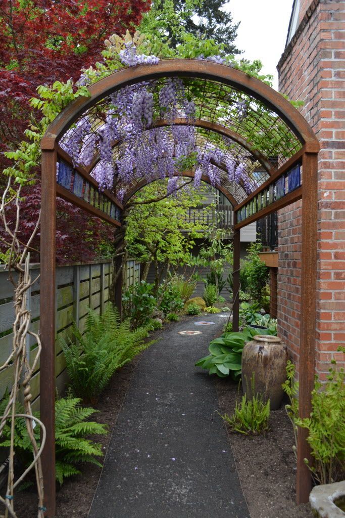 an archway in the middle of a garden with purple flowers growing on it's sides