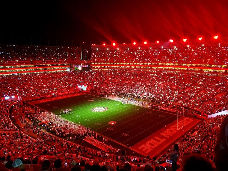 a stadium filled with lots of people watching a football game at night, lit up by bright red lights