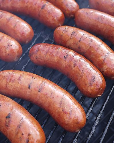 hot dogs and sausages are cooking on the grill