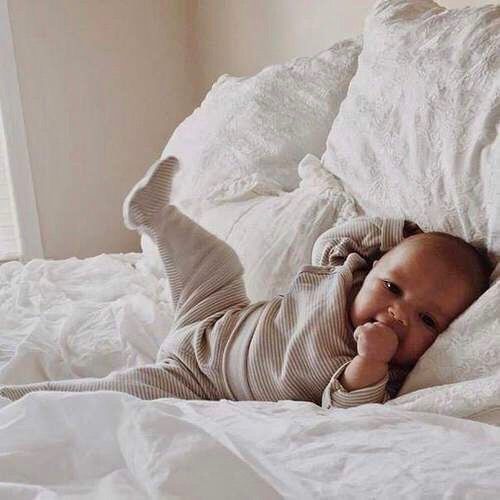 a baby laying on top of a bed with white sheets and pillows in it's arms