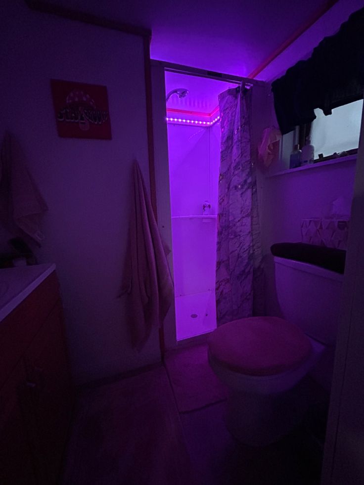 the bathroom is lit up with purple light and has a pink toilet seat in it