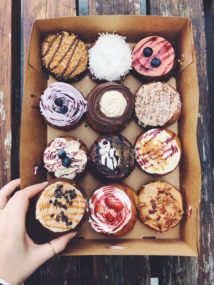 a box filled with lots of different flavored donuts on top of a wooden table