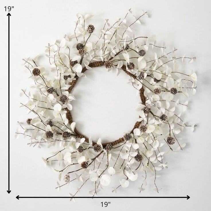 a wreath made out of white flowers and pine cones on a white background with space for text