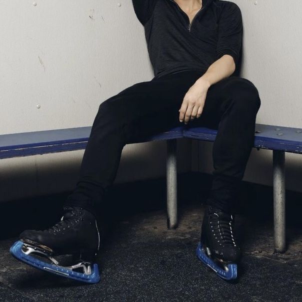 a man sitting on top of a blue bench next to a white wall and wearing black shoes