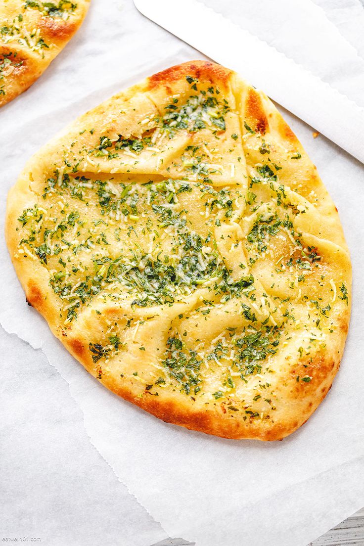 two small pizzas with cheese and herbs on them next to a large white knife