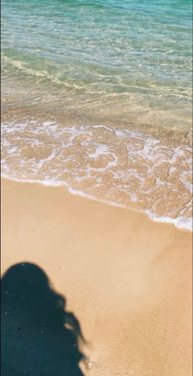 the shadow of a person standing on top of a sandy beach next to the ocean