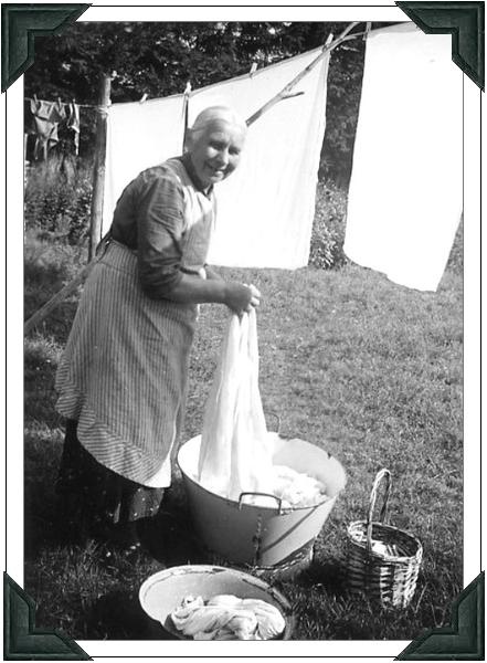 an old black and white photo of a woman washing clothes in a tub on the grass