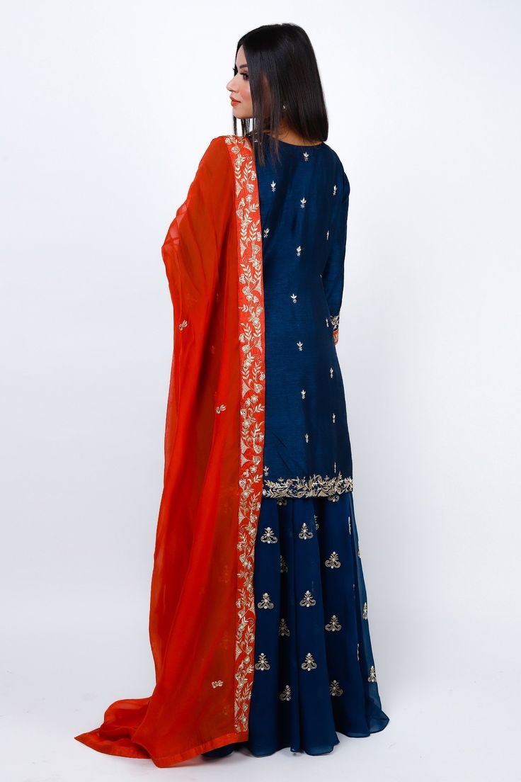 Navy blue kurta featuring zari embroidered floral motifs highlighted with sequin, cut dana and pearls. Comes with sharara and contrasting red dupatta.
Components: 3
Pattern: Embroidered
Type Of Work: Cut dana, Sequin, Zari
Neckline: Round
Sleeve Type: Three quarter
Fabric: Kurta: Slub Silk, Sharara: Georgette, Dupatta: Silk Organza
Color: Blue
Other Details: 
Attached lining
Elasticated waistband
Contrast neck panel
Embroidered pearl detail
Occasion: Mehendi and Haldi,Sangeet - Aza Fashions Silk Sharara, Red Dupatta, Kurta Sharara Set, Kurta Sharara, Blue Kurta, Georgette Dupatta, Sharara Set, Silk Organza, Floral Motifs