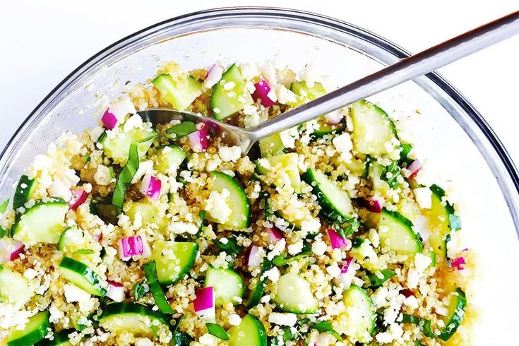 a glass bowl filled with cucumbers, onions and couscous on top of a white table