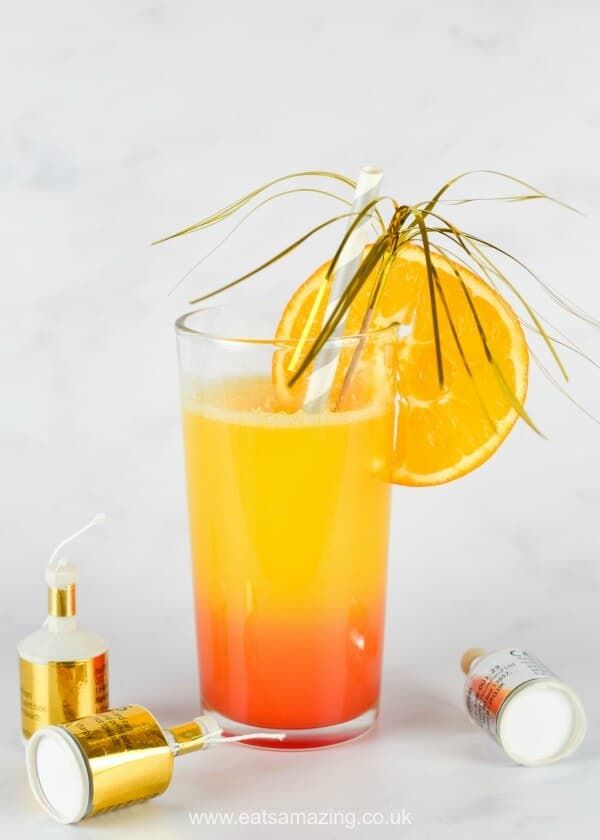 an orange and yellow drink in a glass next to a bottle with some essentials