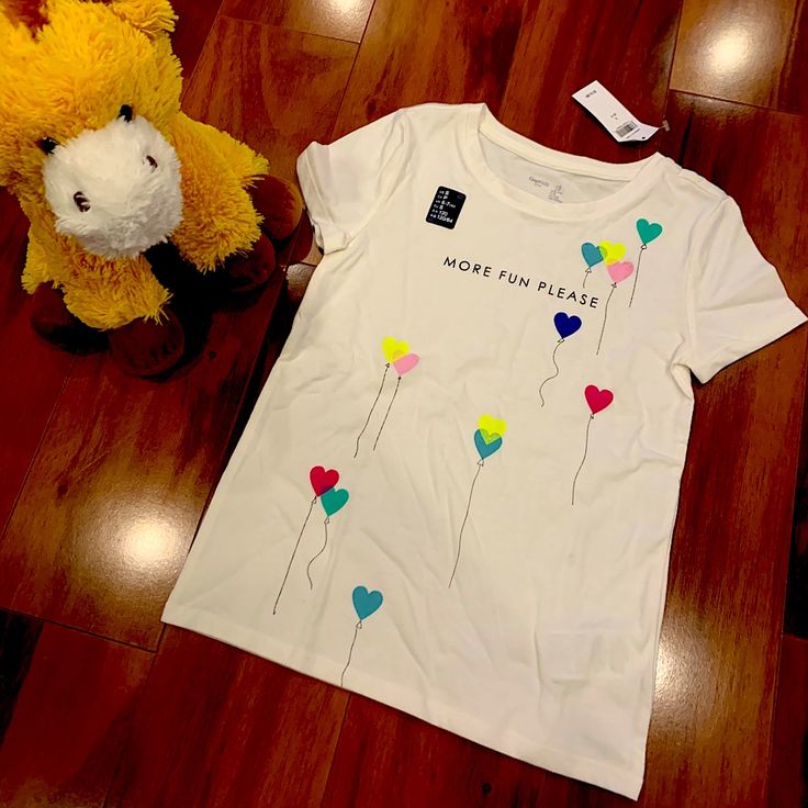 Cute Girls Gap T-Shirt With Multi Colored Heart Balloons Across The Front. Trendy Spring Playtime T-shirt, Trendy Cotton Gap T-shirt, Gap Short Sleeve Tops With Letter Print, Trendy Gap T-shirt For Spring, Playful White Tops With Heart Graphic, Playful White Heart Print Tops, Cute Gap Cotton T-shirt, Gap Graphic Tee For Spring, White Playful T-shirt With Heart Graphic