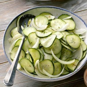 a bowl full of sliced cucumbers and onions with a spoon in it on a wooden table