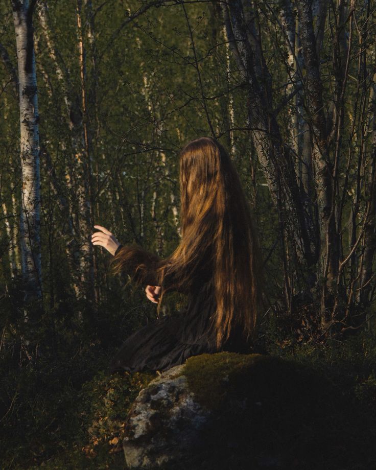 a woman with long hair standing in the woods