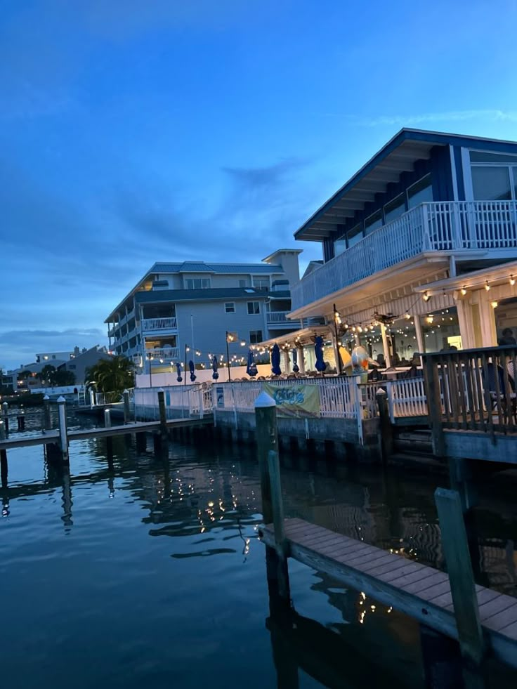 people are sitting at tables on the dock by the water in front of some buildings