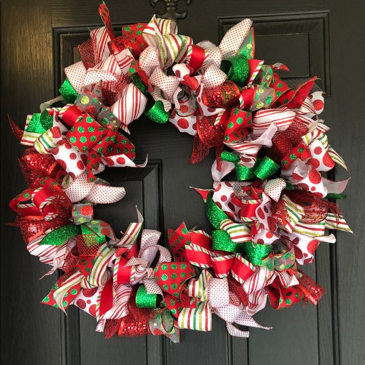 a christmas wreath with red, green and white bows hanging from the front door on a black door