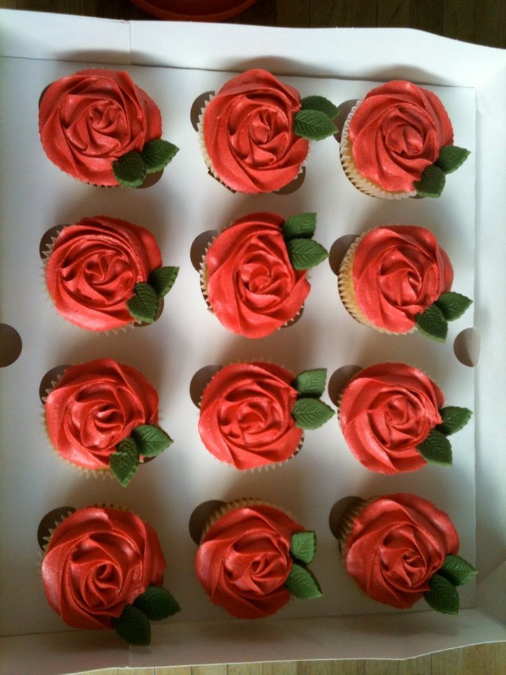 cupcakes with red frosting and green leaves in a white box on a table