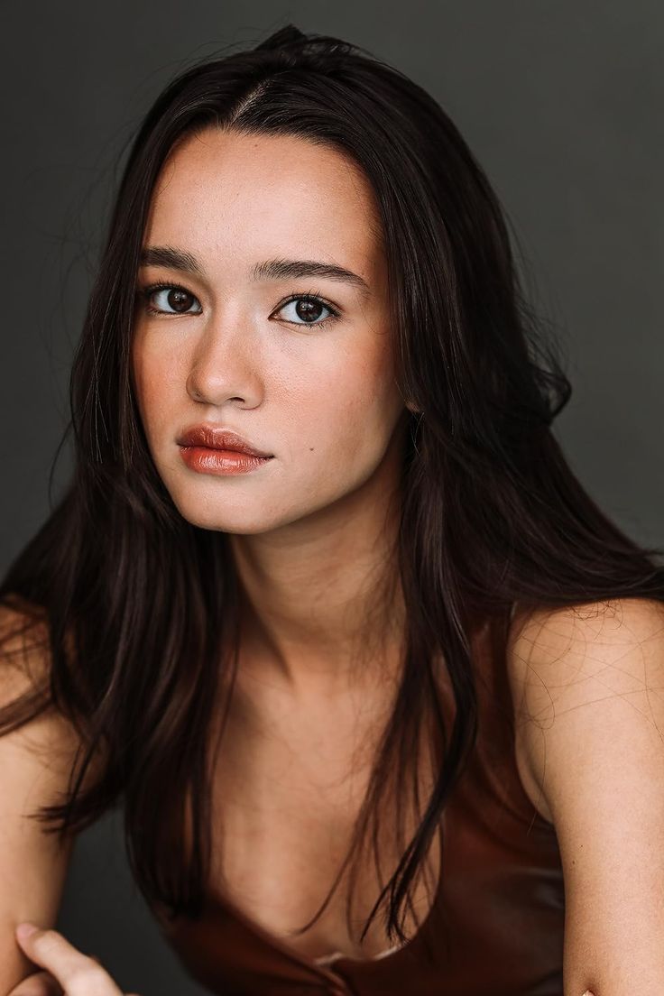 a woman with long dark hair posing for a photo wearing a brown dress and looking at the camera