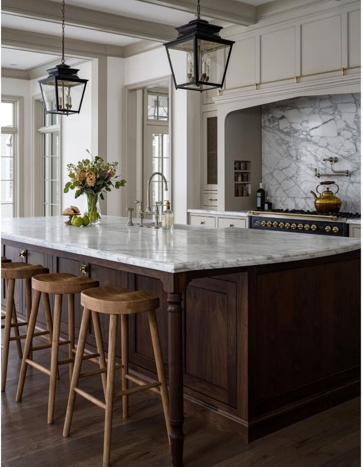 a kitchen island with three stools in front of it and two lights hanging from the ceiling