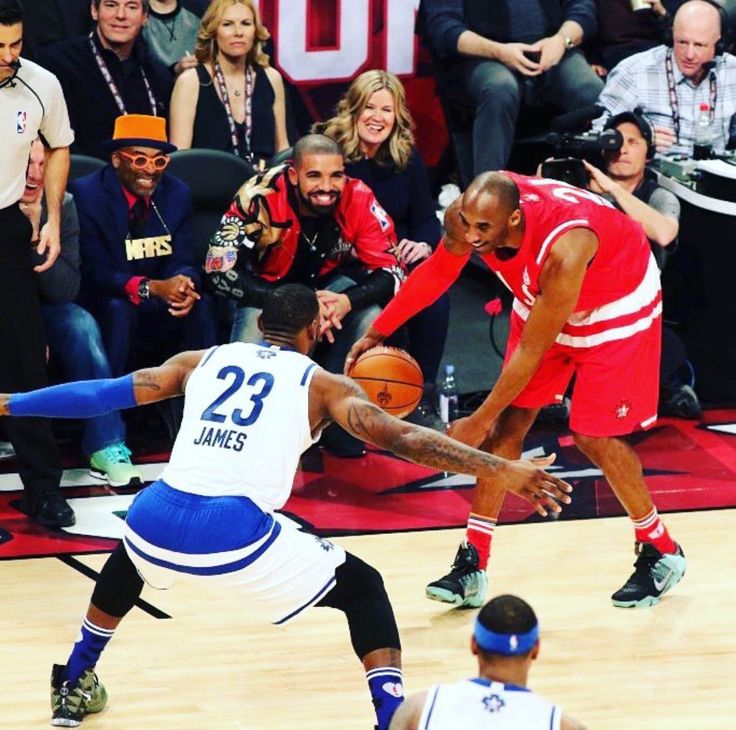 two men playing basketball in front of an audience at a sporting event, one is dribbling the ball