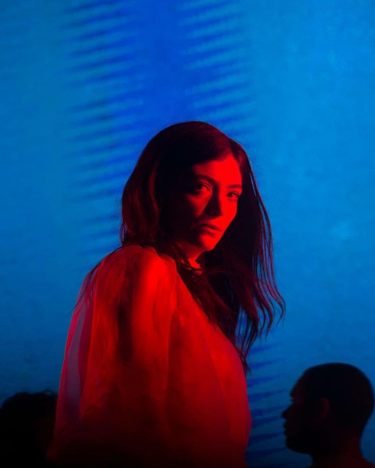 a woman standing in front of a blue wall with red light on it's face