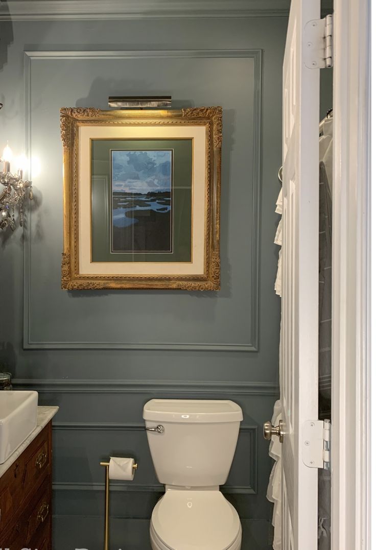 a white toilet sitting in a bathroom next to a sink under a framed picture on the wall