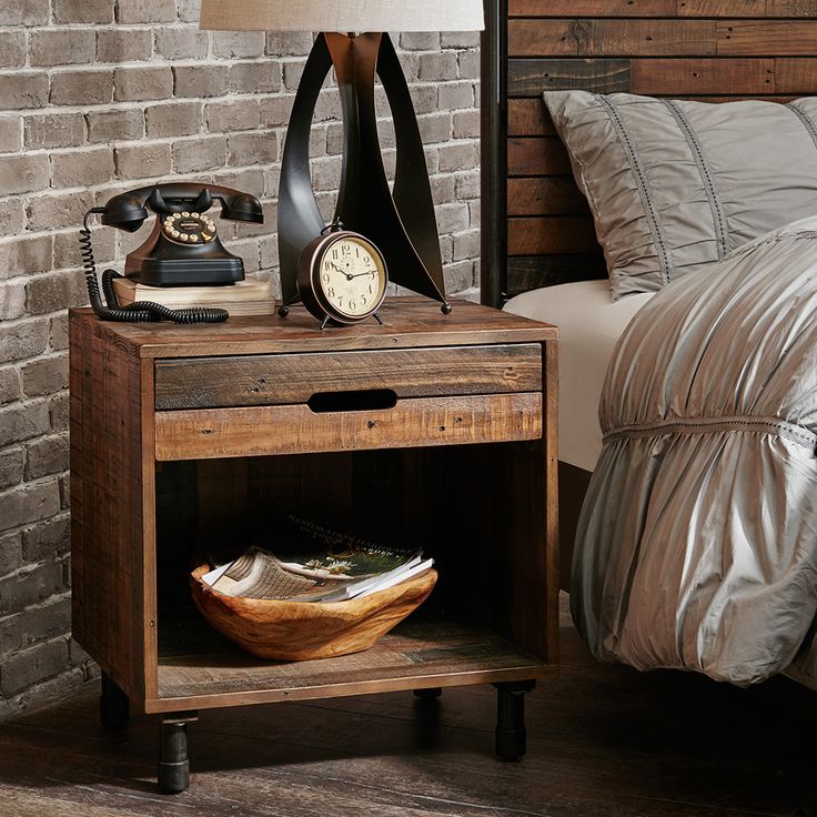 a bed with a wooden night stand next to a brick wall