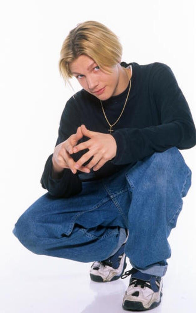 a young man sitting on the ground with his hands together and looking at his cell phone