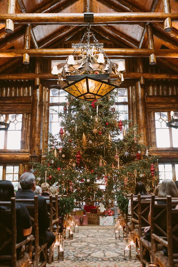 a large christmas tree is in the middle of a room with pews and candles