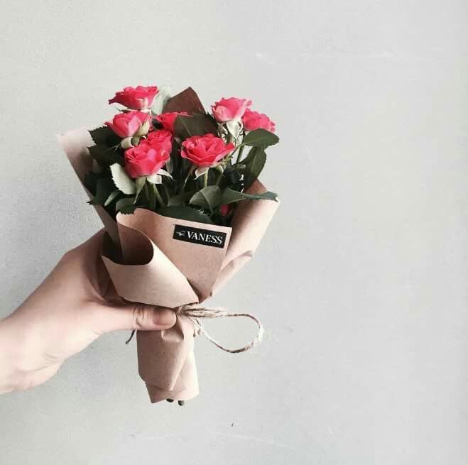 a person holding a bouquet of flowers wrapped in brown paper and tied with twine