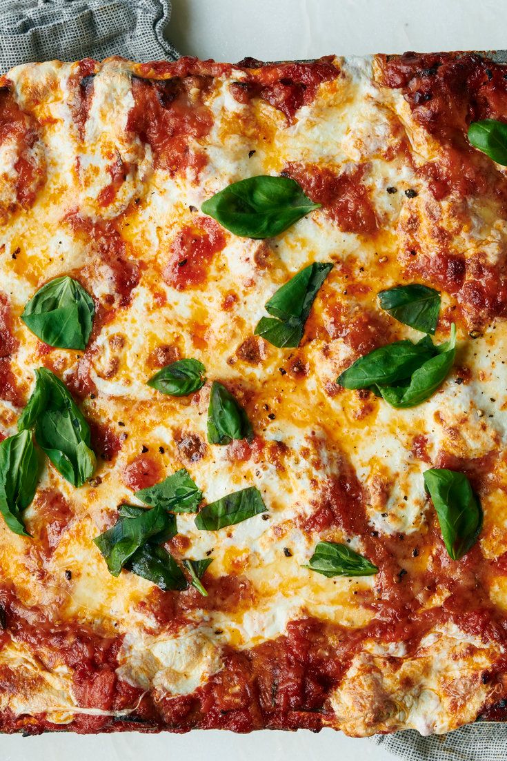 a square pizza covered in cheese and basil leaves on top of a white table cloth