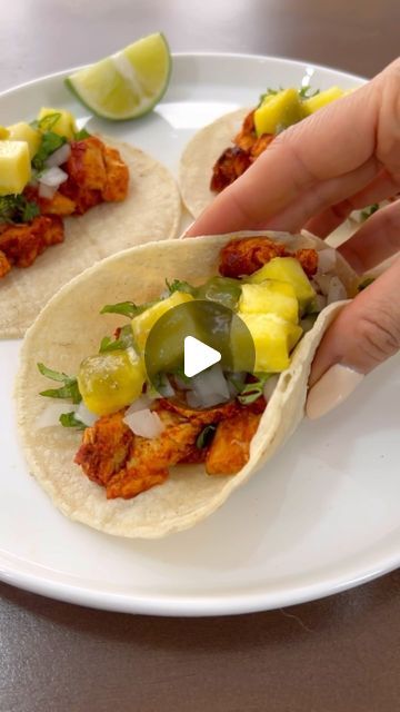 two tacos on a white plate being held by someone's hand with a lime wedge in the middle